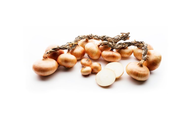 Varias cebollas de Betanzos enteras con trenzas secas y algunas cortadas mostrando su interior blanco